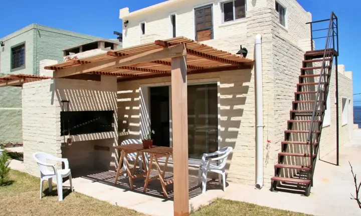 Pérgola con mesa y parrillero junto a la casa